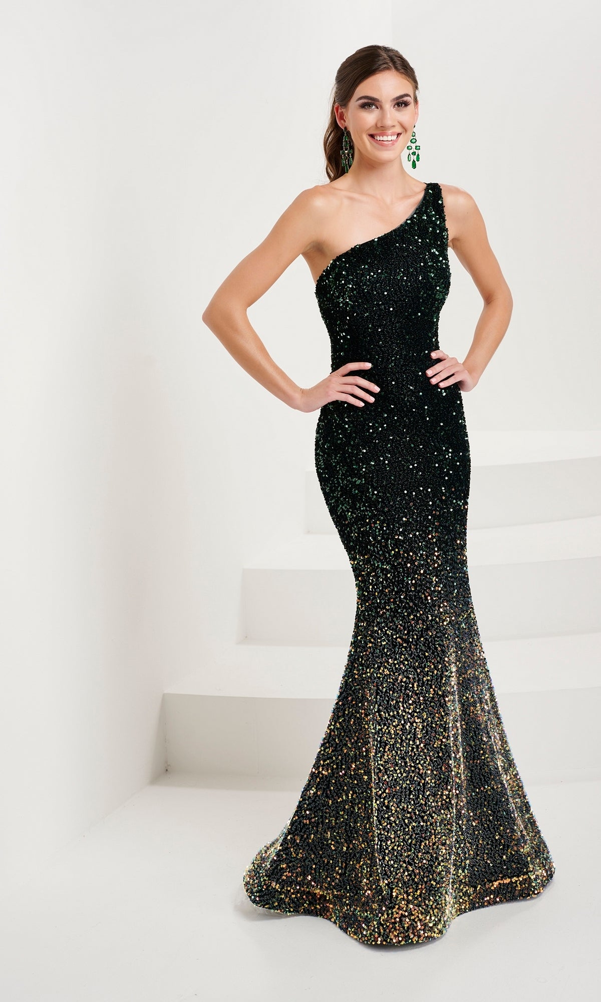 A woman poses in the Tiffany Ombre Sequin Mermaid Prom Dress 16089, featuring a black, one-shoulder design with a fitted silhouette and strappy open back, standing by steps on a white background.